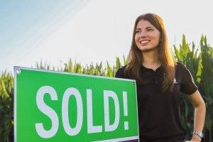 A DreamDirt representative smiles with a Sold Sign.