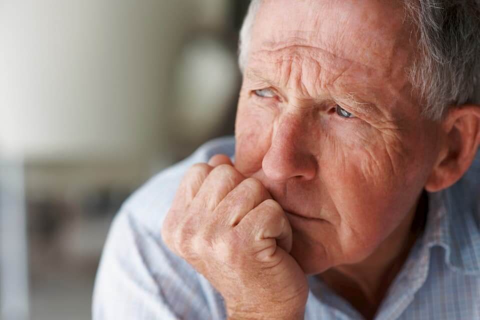 A man with gray hair and wrinkles looks pensive.