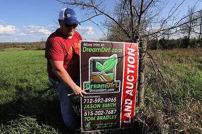 A man places a land auction sign beside a field.