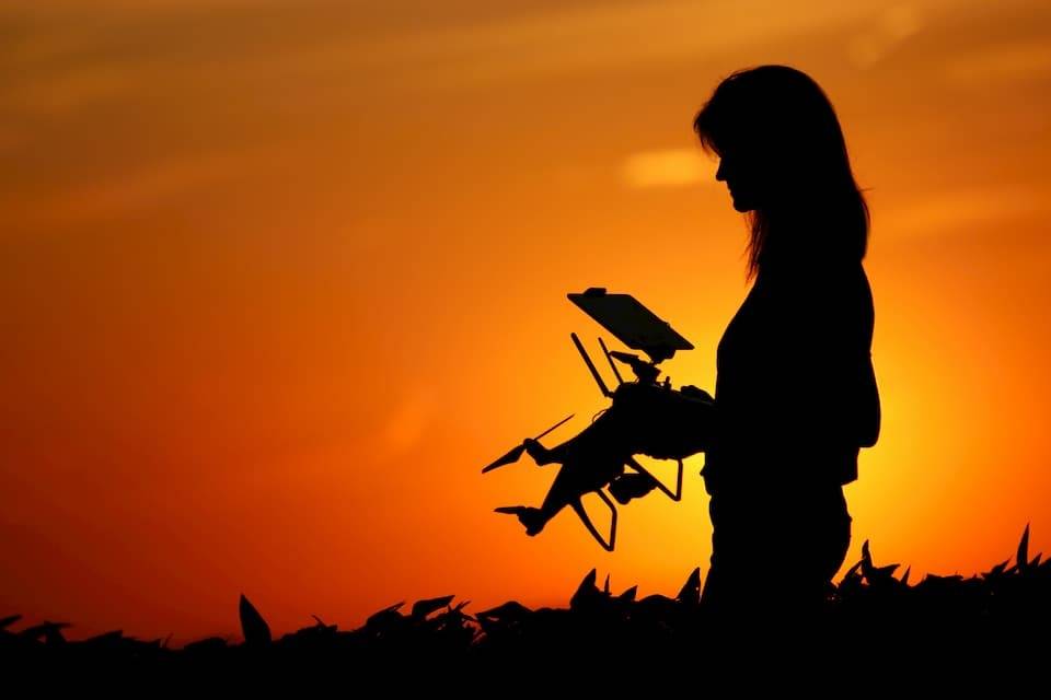 A female auctioneer's silhouette holding a drone as the sun sets in the background.