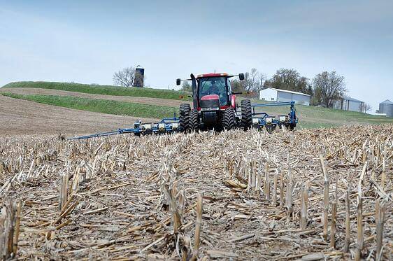 Photo of an oncoming tractor pulling farm equipment over a field.