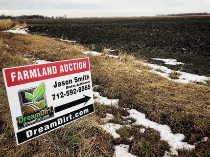 A Farmland Auction sign on the side of a road points passers-by towards the correct direction of an auction.